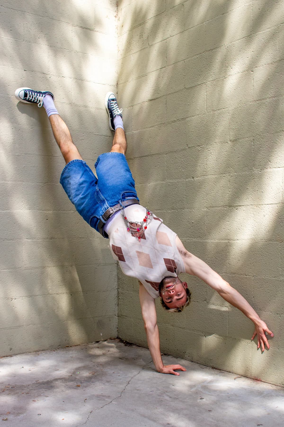 Jeffrey balancing upside down on one hand against a sunlit wall
