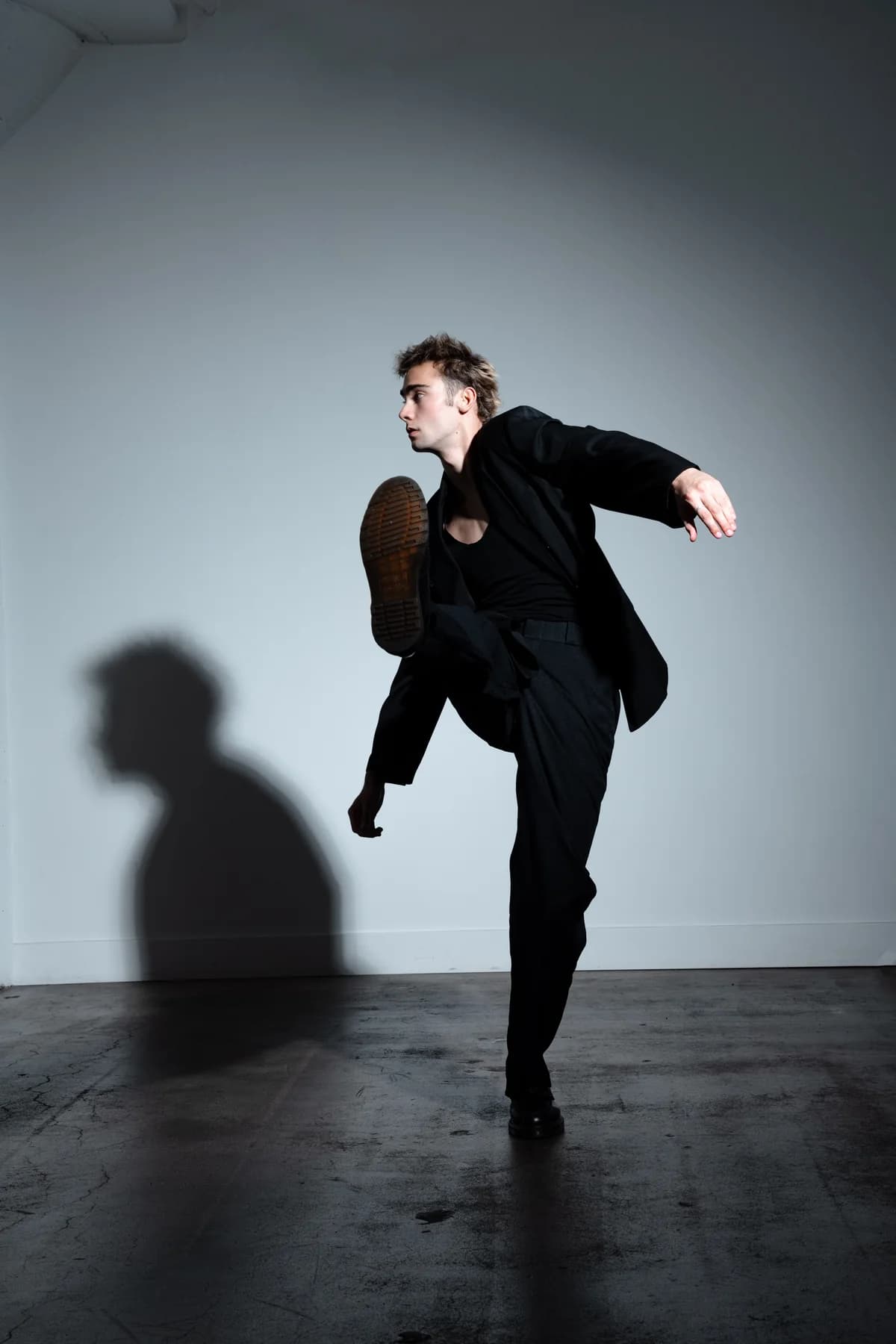 Jeffrey balancing in a high kick in a black suit