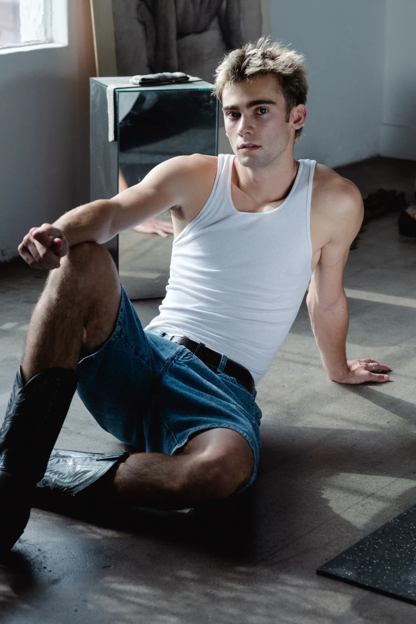 Jeffrey seated in a white tank and blue shorts in window light